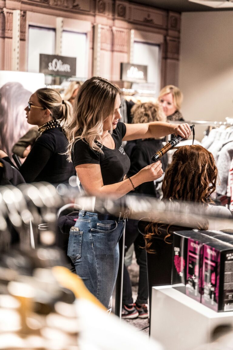 Eine junge Friseurin lernt gerade an einem Puppenkopf, wie man Locken mit einem Lockenstab zaubert.